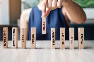 businesswoman pulling wooden dominos with the words "Brand" "Marketing" "Advertising" "Logo" and "Design" on them