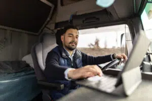 a truck driver typing an address into his tablet while sitting in the cab of his truck